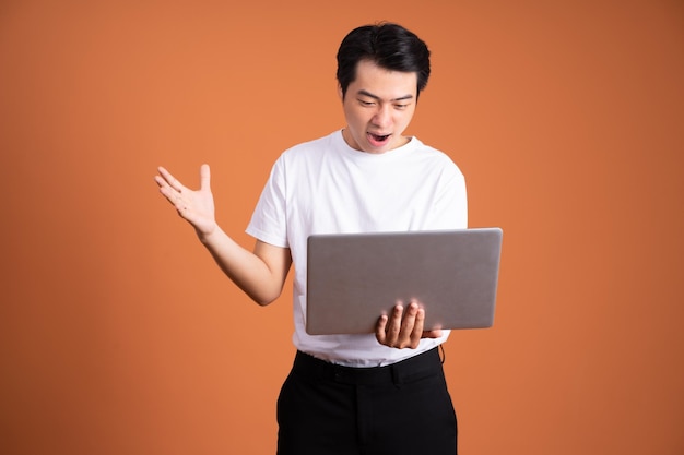 Asiatischer Mann mit Laptop isoliert auf orangefarbenem Hintergrund