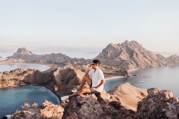 Asiatischer Mann mit Sonnenbrille sitzt auf dem Felsen und blickt auf die Insel Padar