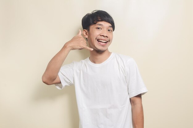 Asiatischer mann mit weißem t-shirt und telefongeste mit den händen auf isoliertem hintergrund