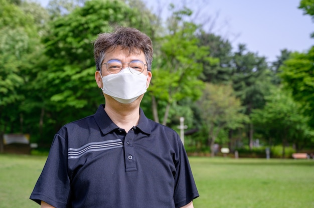 Asiatischer Mann mittleren Alters, der eine Gesichtsmaske auf dem Rasen trägt.