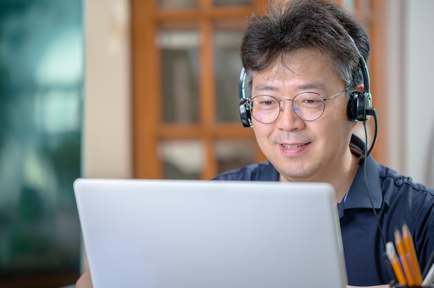 Asiatischer Mann mittleren Alters, der zu Hause arbeitet. Telearbeitskonzept.