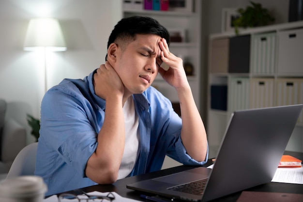 Asiatischer Mann müde von harter Arbeit mit geschlossenen Augen mit Laptop, um von zu Hause aus zu arbeiten