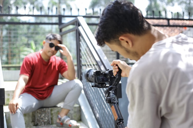 Asiatischer Mann posiert für das Filmen von Vlogging im Freien. Videofilmer, der Gimbal mit Kamera hält.