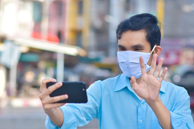 Asiatischer Mann ruft Telefon in der medizinischen Maske auf Straße in der Stadt an