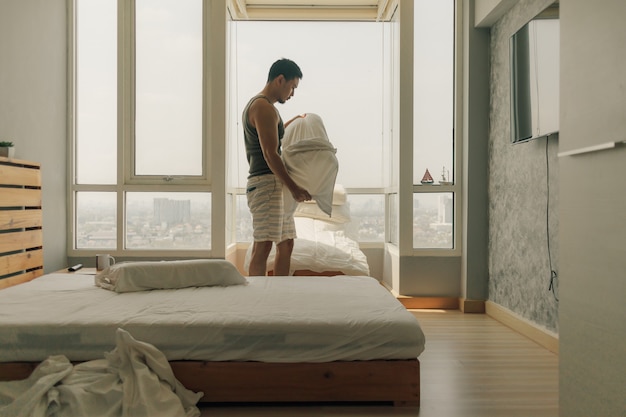 Asiatischer Mann säubert sein Schlafzimmer mit warmem Sommerlicht.