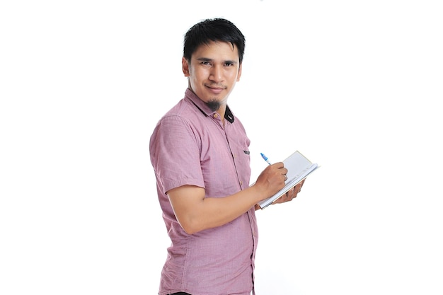 Asiatischer Mann schreibt auf seinem Tagebuch mit rosa T-Shirt isoliert auf weißem Hintergrund