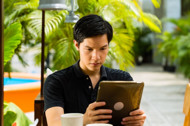 Asiatischer Mann sitzt in einer Bar oder in einem Café im Freien