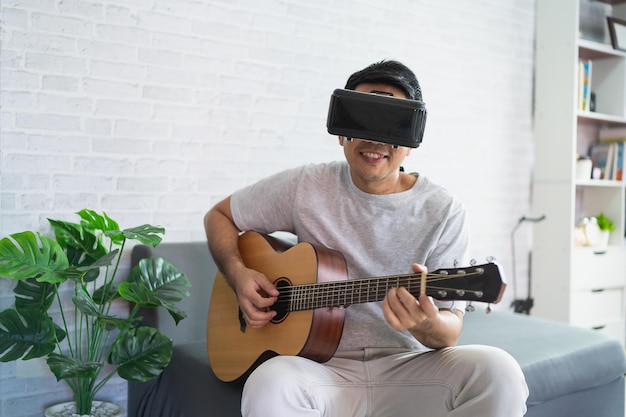 Asiatischer Mann spielt Gitarre, singt Lied und spielt VR-Spiel, um zu Hause zu unterhalten. Asiatischer Mann, fröhlich im Haus im Urlaub