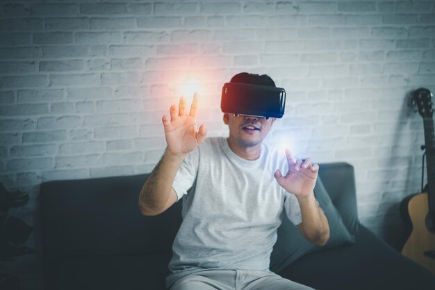 Asiatischer Mann spielt VR-Spiel, um zu Hause zu unterhalten, asiatischer Mann, der im Urlaub im Haus fröhlich ist. Glücklicher Mann, der Metaverse VR-Technologiekonzept spielt.