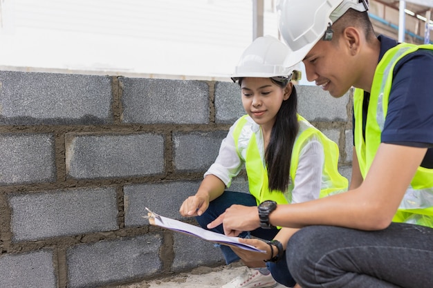 Foto asiatischer mann und frau bauingenieur papierplan gebäudearchitekt tragen weißen sicherheitshelm blick auf baustelle.