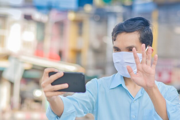 Asiatischer Mann verwenden Gesichtsmaske Videoanrufkonferenz auf Straße in der Stadt neues normales soziales Distanzierungskonzept