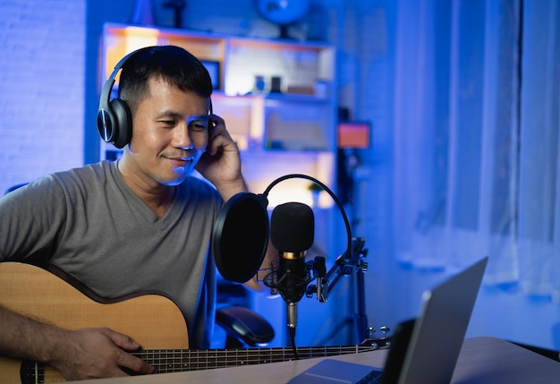 Asiatischer mann youtuber live-streaming-performance gitarre spielen und ein lied singen asiatischer mann unterrichtet gitarre und singt online musiker nimmt musik mit laptop auf und spielt akustikgitarre