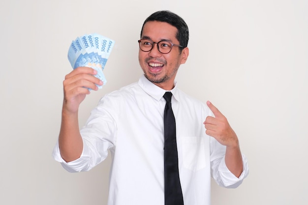 Asiatischer Mann zeigt aufgeregten Gesichtsausdruck, wenn er auf das Geld zeigt, das er in der Hand hält