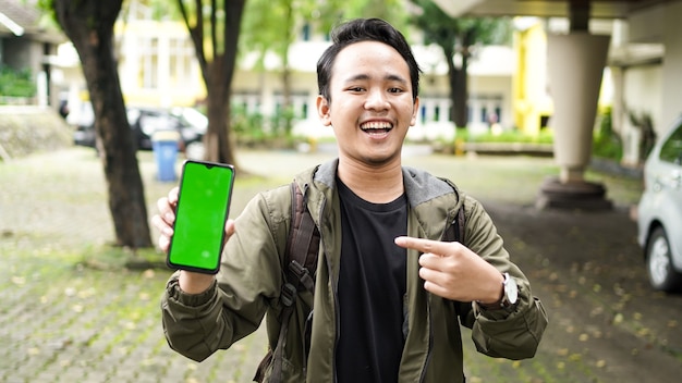 Asiatischer Mann zeigte mit einem Lächeln auf das Green-Screen-Handy
