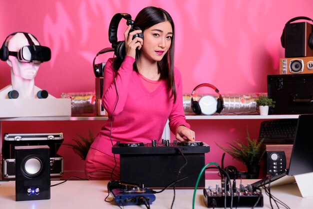 Asiatischer Musiker spielt nachts im Club Technomusik mit einer professionellen Mischkonsole und hat während des Konzerts Spaß mit den Fans. DJ-Künstler mit rosa Bluse mischt elektronische Sounds im Studio