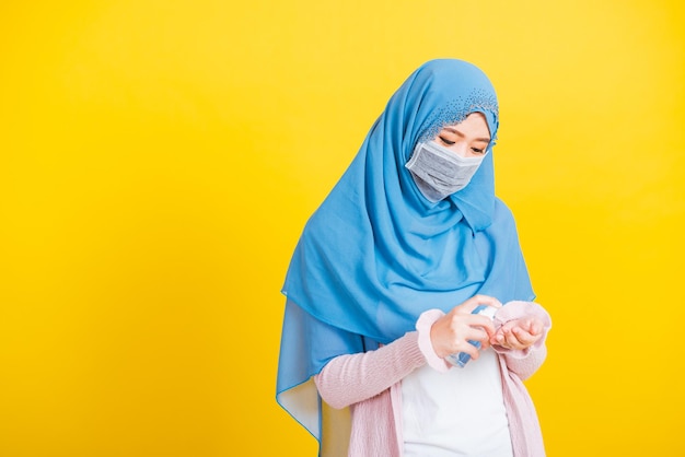 Asiatischer muslimischer Araber, Porträt einer glücklichen, schönen jungen Frau, die den Islam religiös trägt, Schleier, Hijab und Gesichtsmaske, schützt sie vor der Quarantäne der Krankheit Coronavirus, wenden Alkoholspray auf die Hände an, isoliert gelb