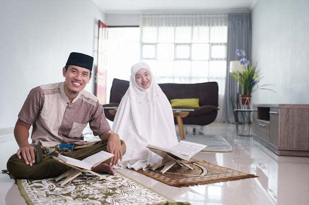 Asiatischer muslimischer Mann, der Frau unterrichtet, die Koran oder Koran im muslimischen Wohnzimmerpaar liest, das zu Hause betet