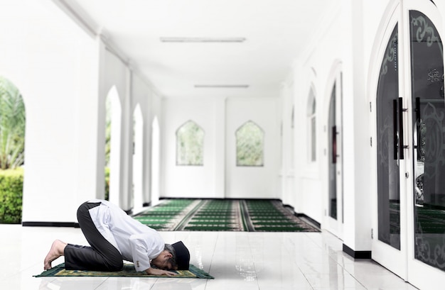 Asiatischer muslimischer Mann mit einem Gebetsteppich in einer betenden Position (salat)