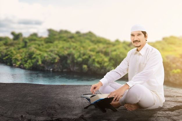 Asiatischer muslimischer mann sitzt und liest den koran mit im freien