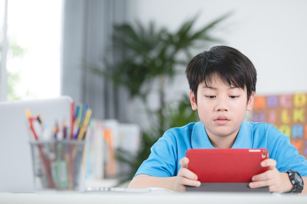 Asiatischer netter Junge, der Tablet-Computer verwendet.