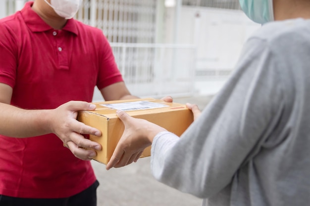 Foto asiatischer online-shopping-lieferant mit gesichtsmaske tragen ein paket an den kunden liefern