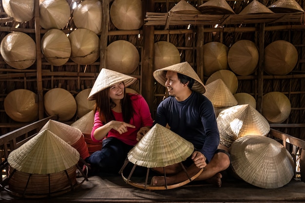 Asiatischer Paarreisendenhandwerker, der den traditionellen Vietnam-Hut im alten traditionellen Haus macht