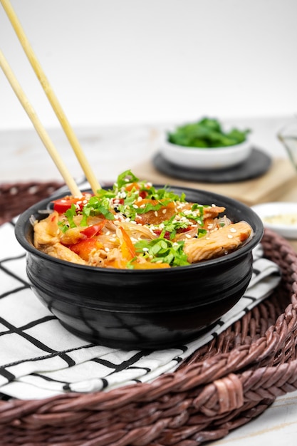 Asiatischer Salat mit Reisnudeln, Gemüse, Champignons, Hühnerfleisch und Sojasauce. Funchose mit weißen transparenten Nudeln im schwarzen Teller