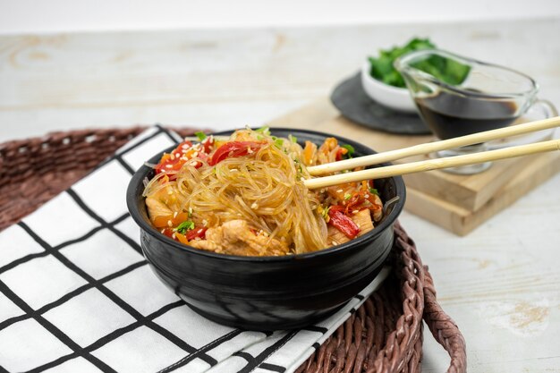 Asiatischer Salat mit Reisnudeln, Gemüse, Champignons, Hühnerfleisch und Sojasauce. Funchose mit weißen transparenten Nudeln im schwarzen Teller