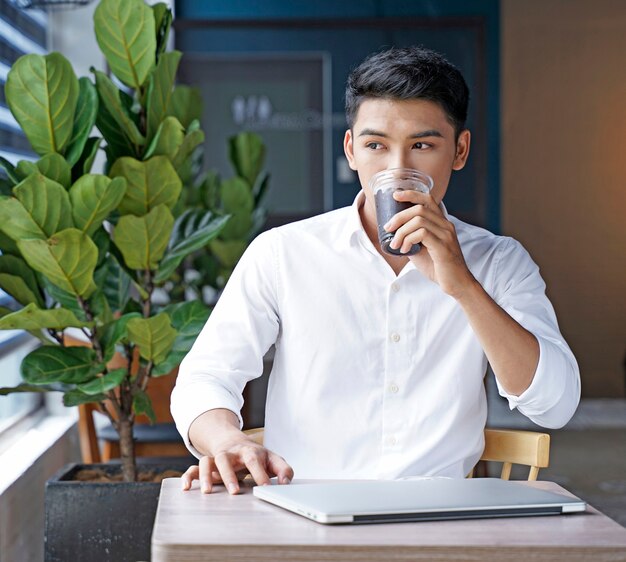 Asiatischer schöner Geschäftsmann oder Büroangestellter, der am Kaffeehaus arbeitet