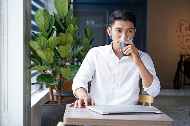 Asiatischer schöner Geschäftsmann oder Büroangestellter, der am Kaffeehaus arbeitet