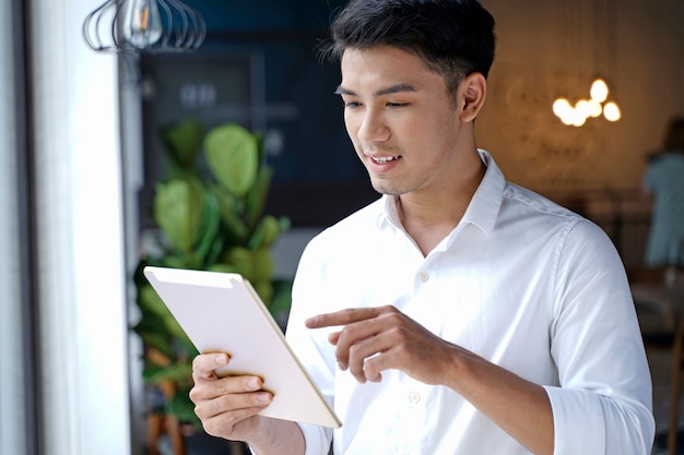 Asiatischer schöner Geschäftsmann oder junger Student, der Pad-Tablet-Computer verwendet