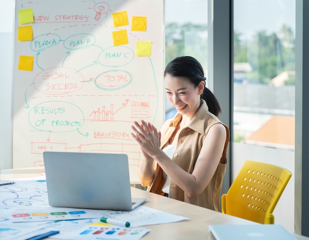 Asiatischer schöner Unternehmer, der Video online mit Laptop und Kartentafel im Büro oder im Schreibtisch arbeitet und spricht