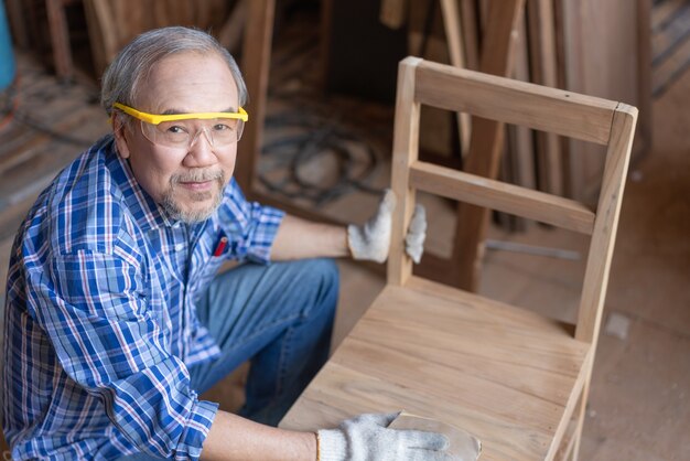 Asiatischer Senior Tischler Mann Schleiffläche auf Holzstuhlmöbeln in der Tischlerei