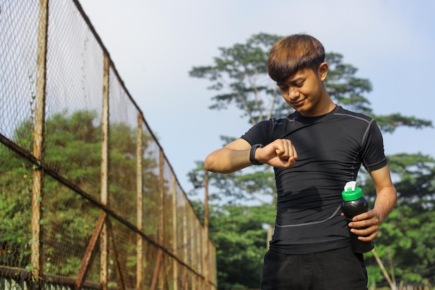 Asiatischer Sportler, der mit Fitnessarmband trainiert und eine Flasche Wasser hält