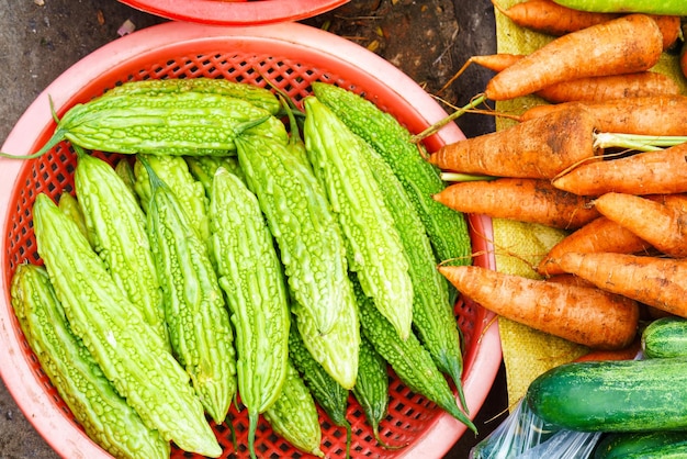 Asiatischer Straßenbauernmarkt, der frisches Obst und Gemüse in Hoi An, Vietnam verkauft. Momordica Charantia oder Bittermelone und Karotte. Hauptsächlich grüne Farben.