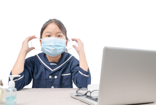 Asiatischer Student, der chirurgische Maske trägt und Computer isoliert, E-Learning und Covid-19- oder Coronavirus-Quarantäne studiert.