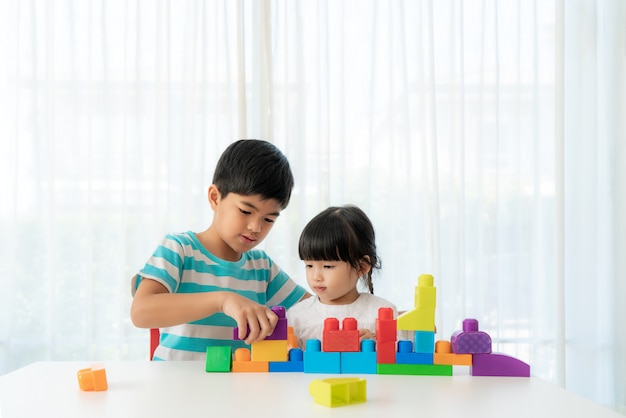 Asiatischer süßer Bruder und Schwester spielen mit einem Spielzeugblockdesigner auf dem Tisch im Wohnzimmer zu Hause.