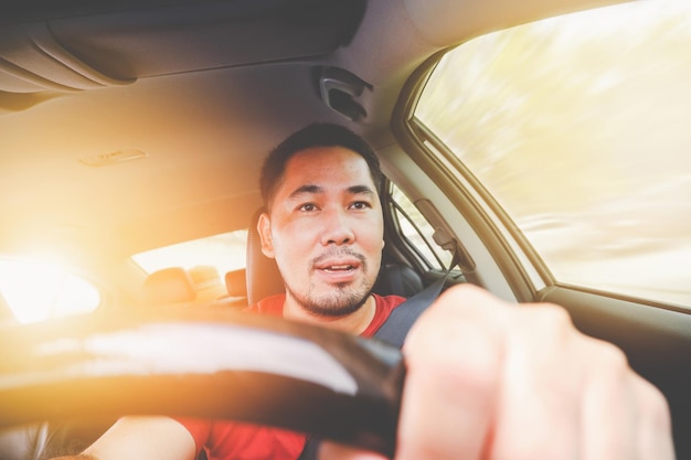 Asiatischer Tourist, der ein Auto fährt, während er einen Gürtel im Sonnenschein im Hintergrund trägt