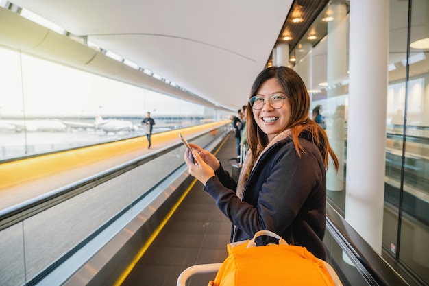 Asiatischer Tourist glücklich und aufgeregt zu reisen, zu gehen und zu lächeln, wenn Sie über Rolltreppe im Flughafen gehen