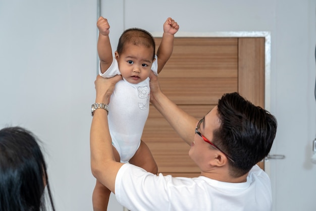 Asiatischer Vater, der das Jungenbaby anhebt Hände und Mutterhand im Haus hält