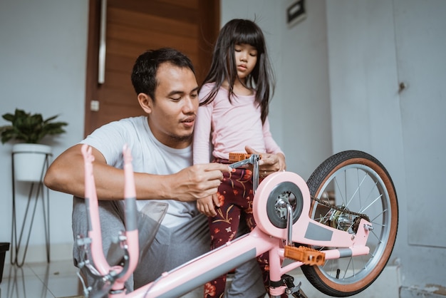 Asiatischer Vater, der mit seiner Tochter ein Fahrradpedal festzieht