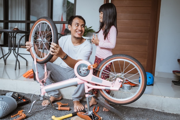 Asiatischer Vater, der mit Tochter ein Fahrrad repariert