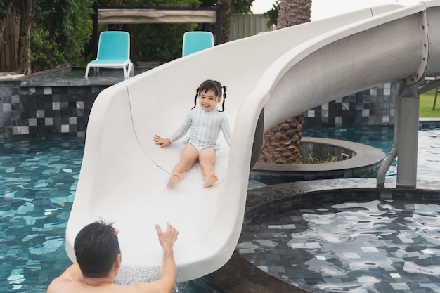 Asiatischer Vater und Tochter schwimmen spielen Rutsche Pool im Pool des Resorts lächelnd und lachen Spaß im Pool im Resort Hotel Familie glückliches Konzept