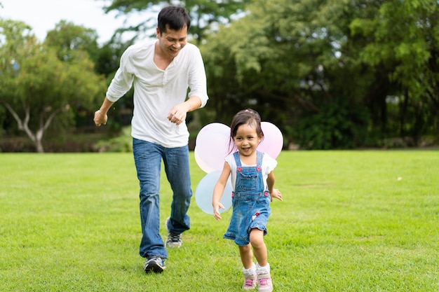 Asiatischer Vater und Tochter spielen die Ballone und laufen zusammen in den Park