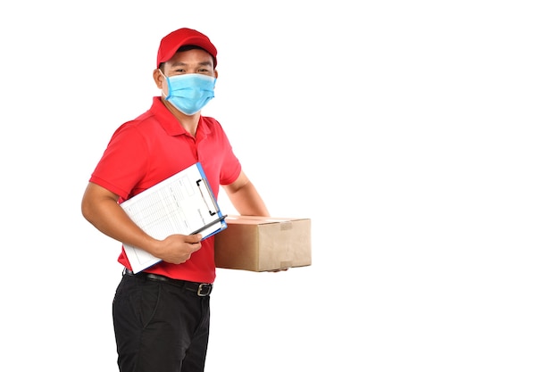 Asiatischer Zusteller, der Gesichtsmaske und Handschuhe in der roten Uniform trägt, die Paketbox lokalisiert auf weißem Hintergrund während des COVID-19-Ausbruchs trägt