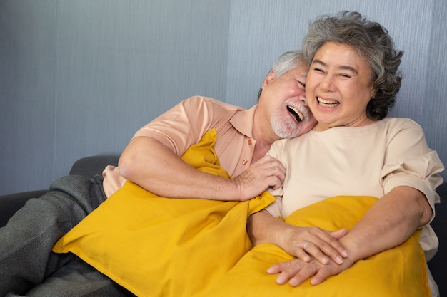 Asiatisches älteres Paar, das lachend auf Sofa zu Hause sitzt.