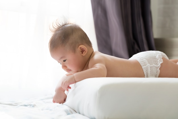 Asiatisches Baby, das auf dem Bauch auf weißem Bett liegt