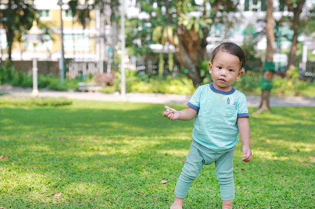 Asiatisches Baby, das ersten Schritt auf Garten des grünen Grases geht.
