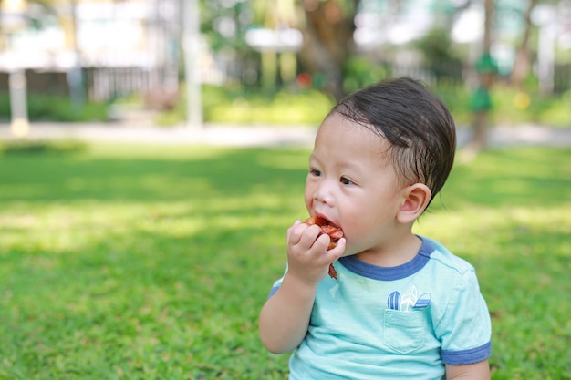 Asiatisches Baby genießen, gebratenes Huhn im grünen Garten zu essen, der im Freien ist.