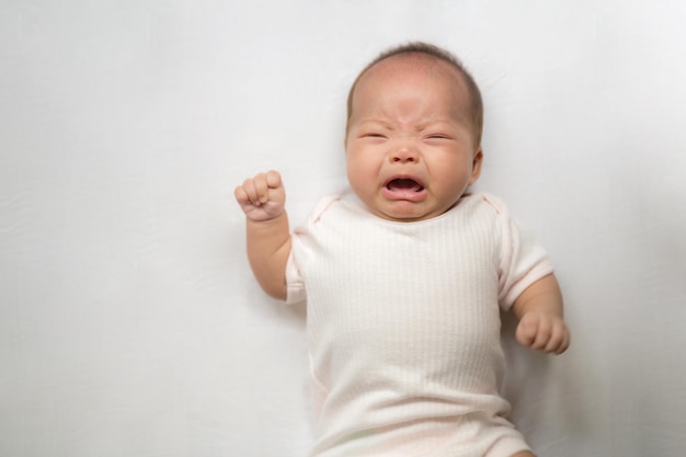 Asiatisches Baby, Säuglingsmädchen weint und schreit auf dem Bett liegend